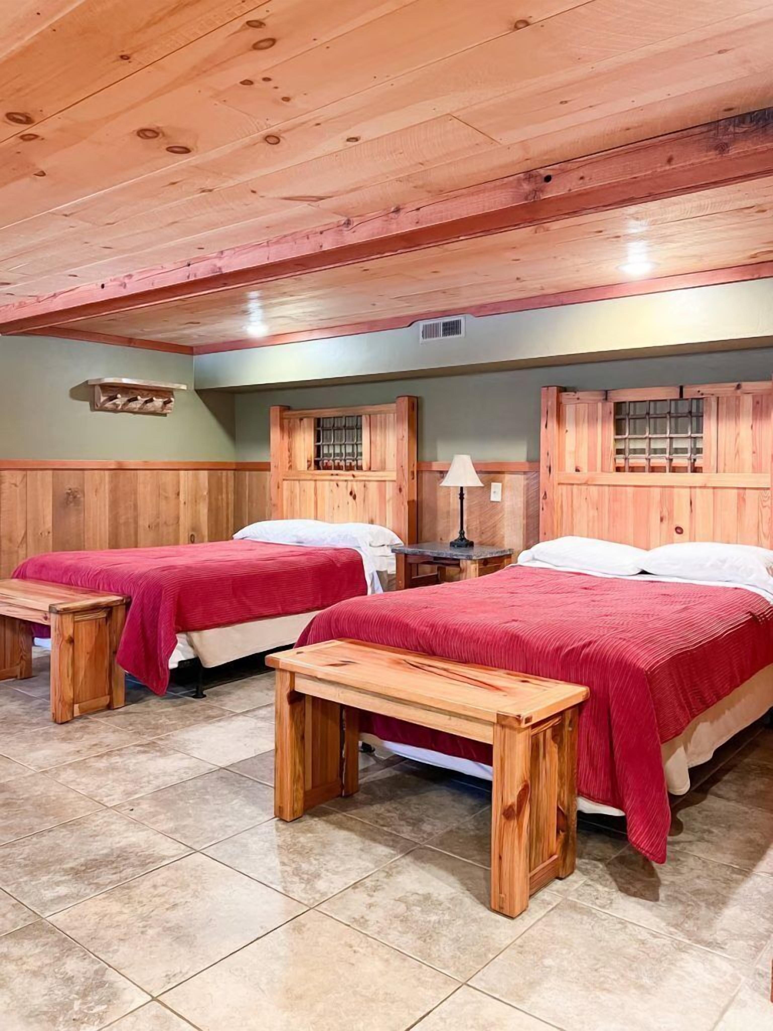 Una habitación con dos camas de madera, cada una con una colcha roja, y un banco de madera frente a cada cama.
