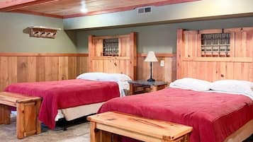 A room with two wooden beds, each with a red bedspread, and a wooden bench in front of each bed.