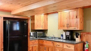 A kitchen with wooden cabinets, a black refrigerator, a microwave, and a coffee maker. - Club 51 (Mercer)