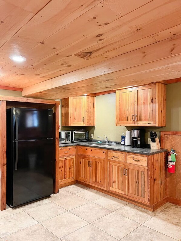 A kitchen with wooden cabinets, a black refrigerator, a microwave, and a coffee maker. - Club 51 (Mercer)