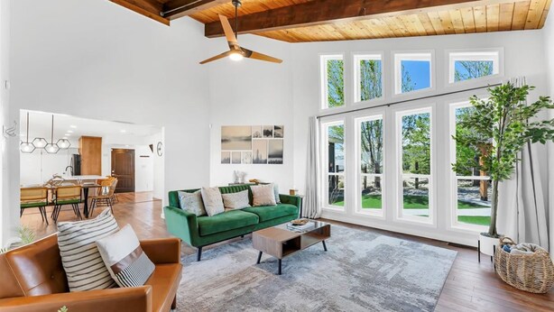 Ein geräumiges Wohnzimmer mit einem grünen Sofa, einem braunen Ledersessel und einem Couchtisch. Es gibt einen Essbereich mit Tisch und Stühlen, und eine Küche ist im Hintergrund zu sehen.