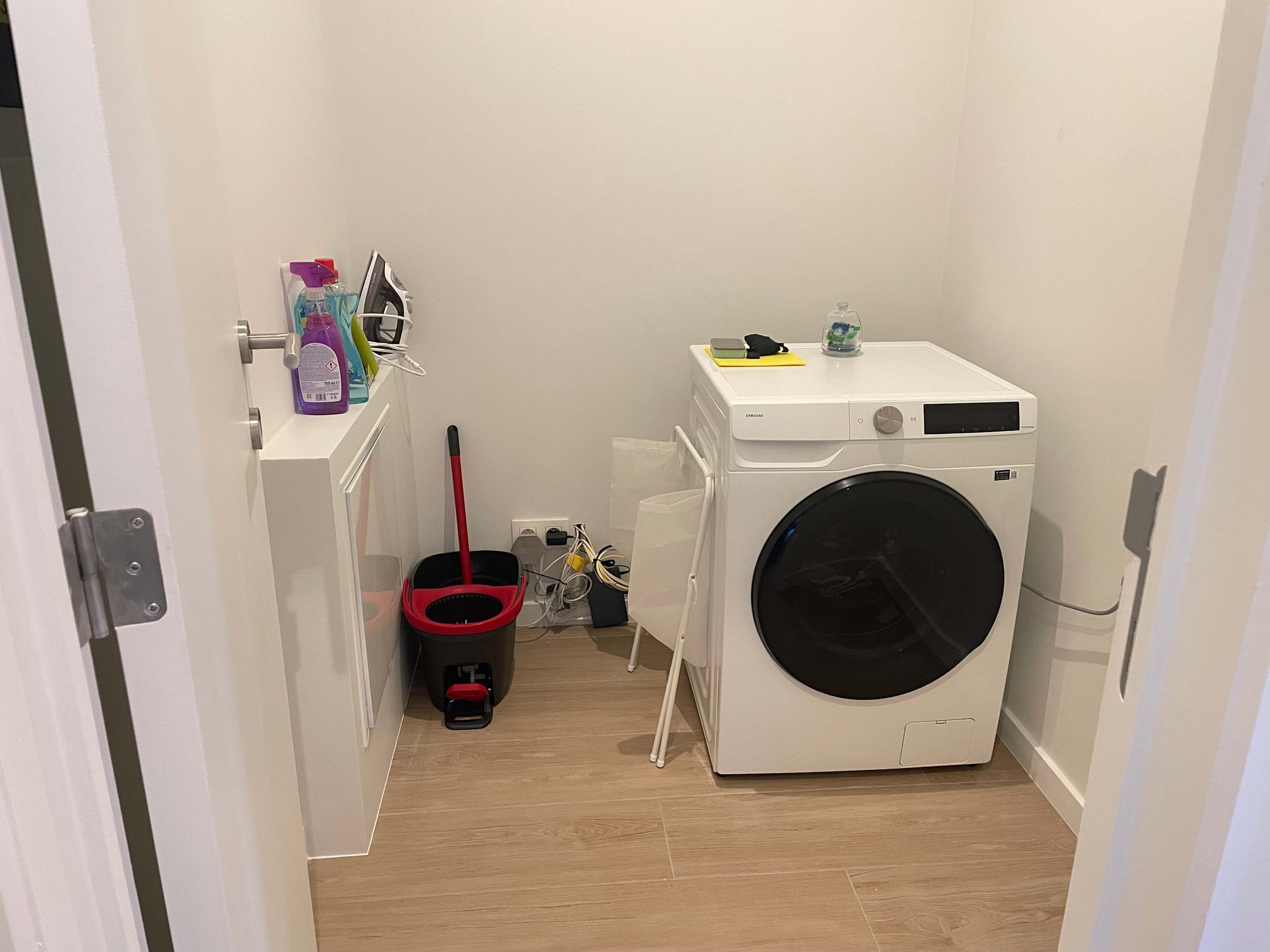 A laundry room with a front-loading washing machine, a mop, and cleaning supplies.