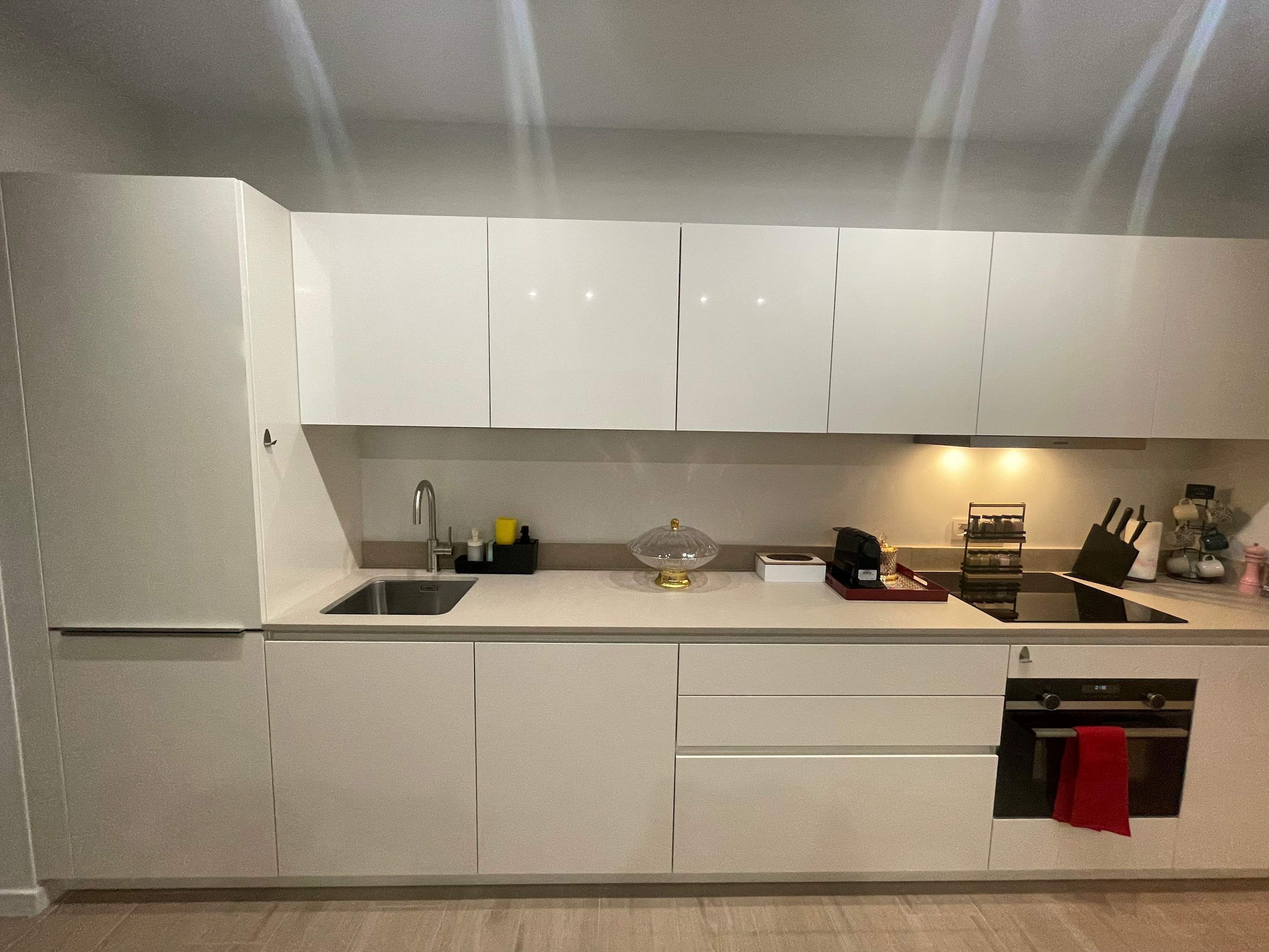 Eine moderne Küche mit weißen Schränken, einer Edelstahl-Spüle, einem eingebauten Backofen und einem roten Handtuch, das an der Backofentür hängt.