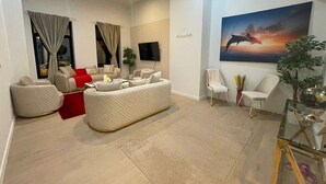 A living room with a sofa, chairs, a TV, and a painting of a dolphin. - One Lux Stay Near Antwerp Central Grande Deluxe 3 Bedroom Suite (Antwerp)