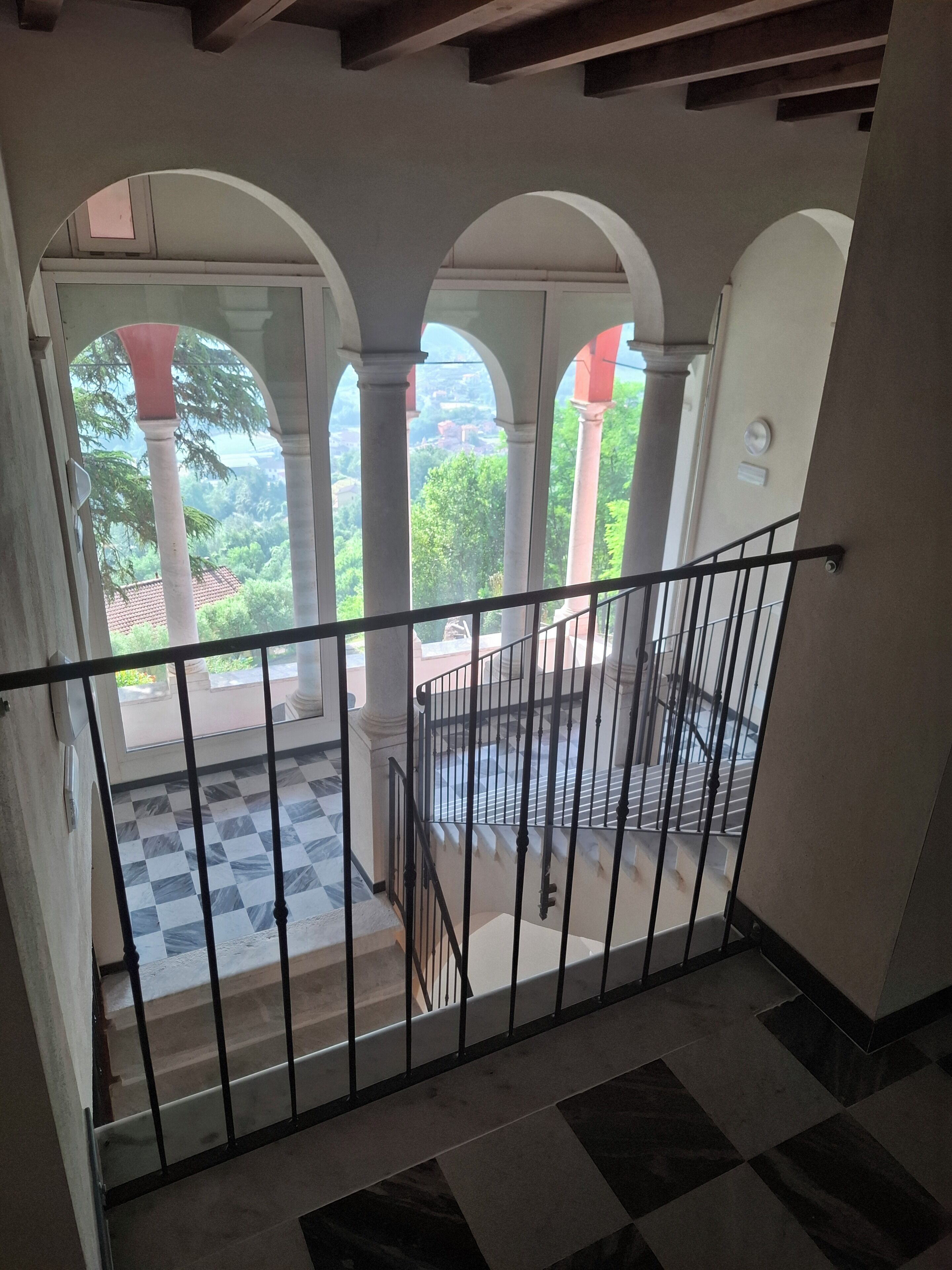 Un escalier avec une rampe en métal noir menant à un espace extérieur agrémenté d’arcades et doté d’un sol à carreaux.