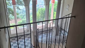 Un escalier avec une rampe en métal noir menant à un espace extérieur agrémenté d’arcades et doté d’un sol à carreaux.