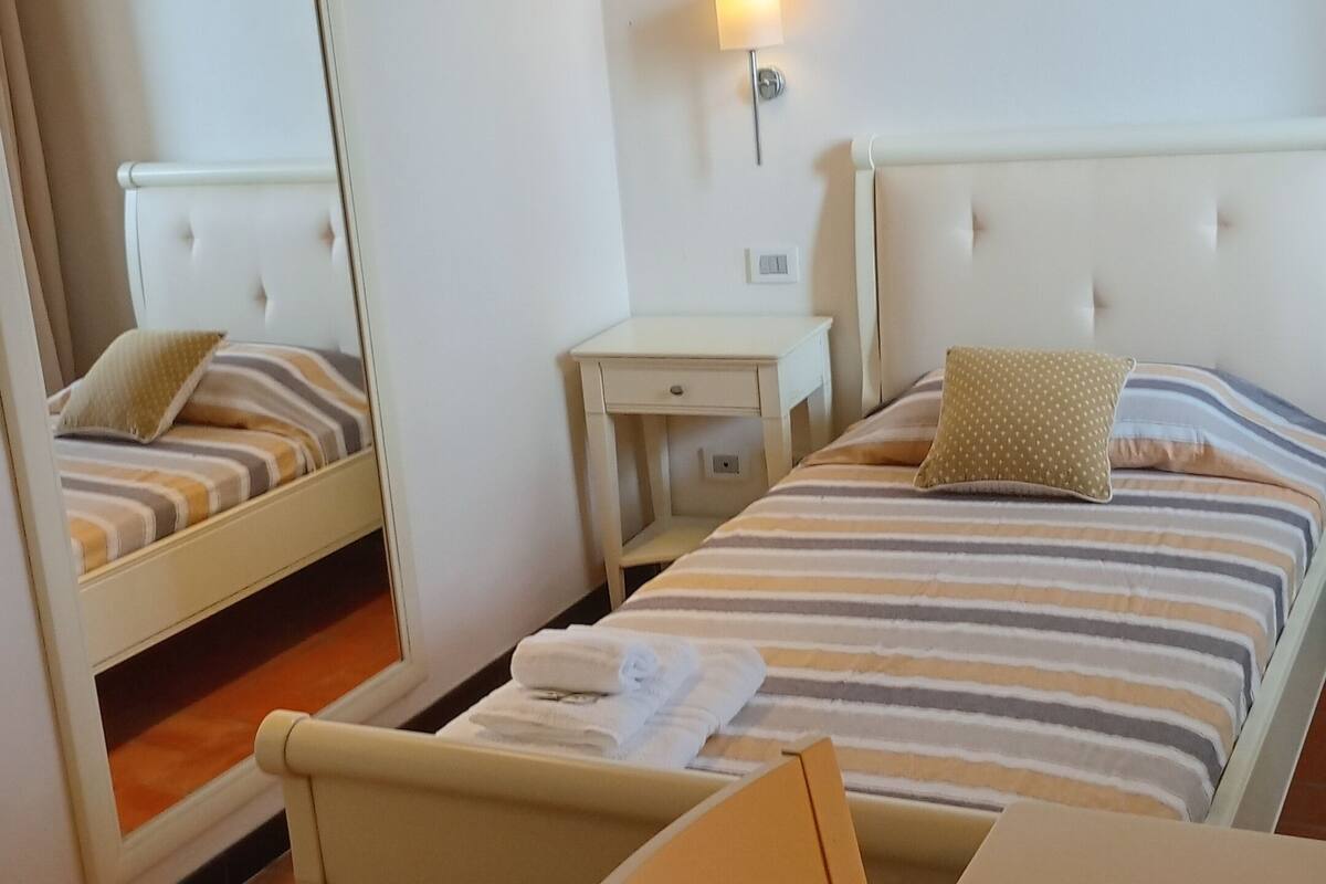 Hotellihuone, jossa on sänky, työpöytä, tuoli, yöpöytä ja peili.