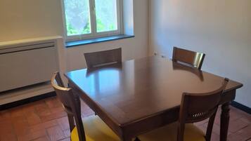 A dining table with four chairs, a window with a view of greenery, and a radiator on the wall.