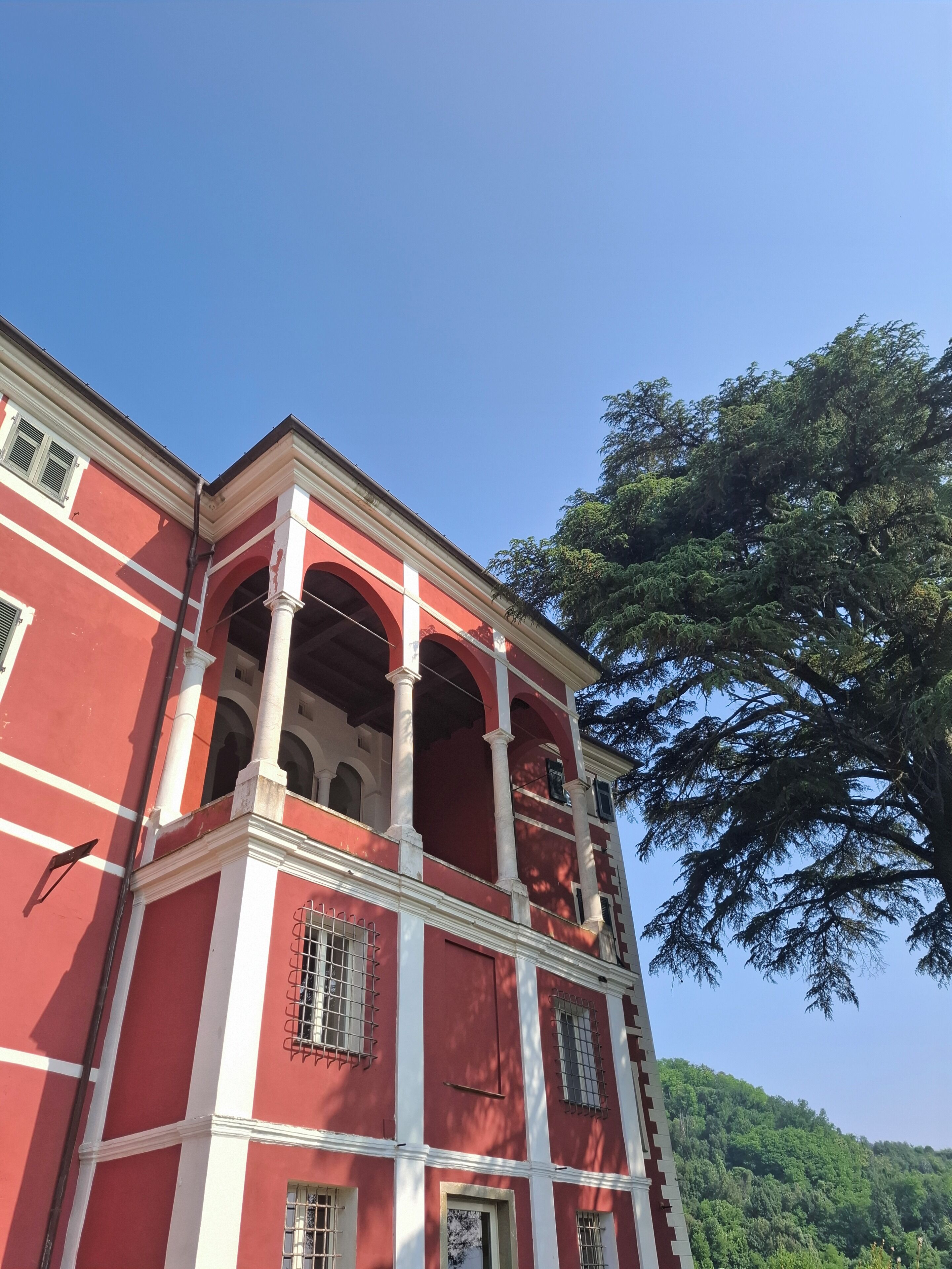 A red building with white trim and multiple windows, including a balcony with a tree in the background.