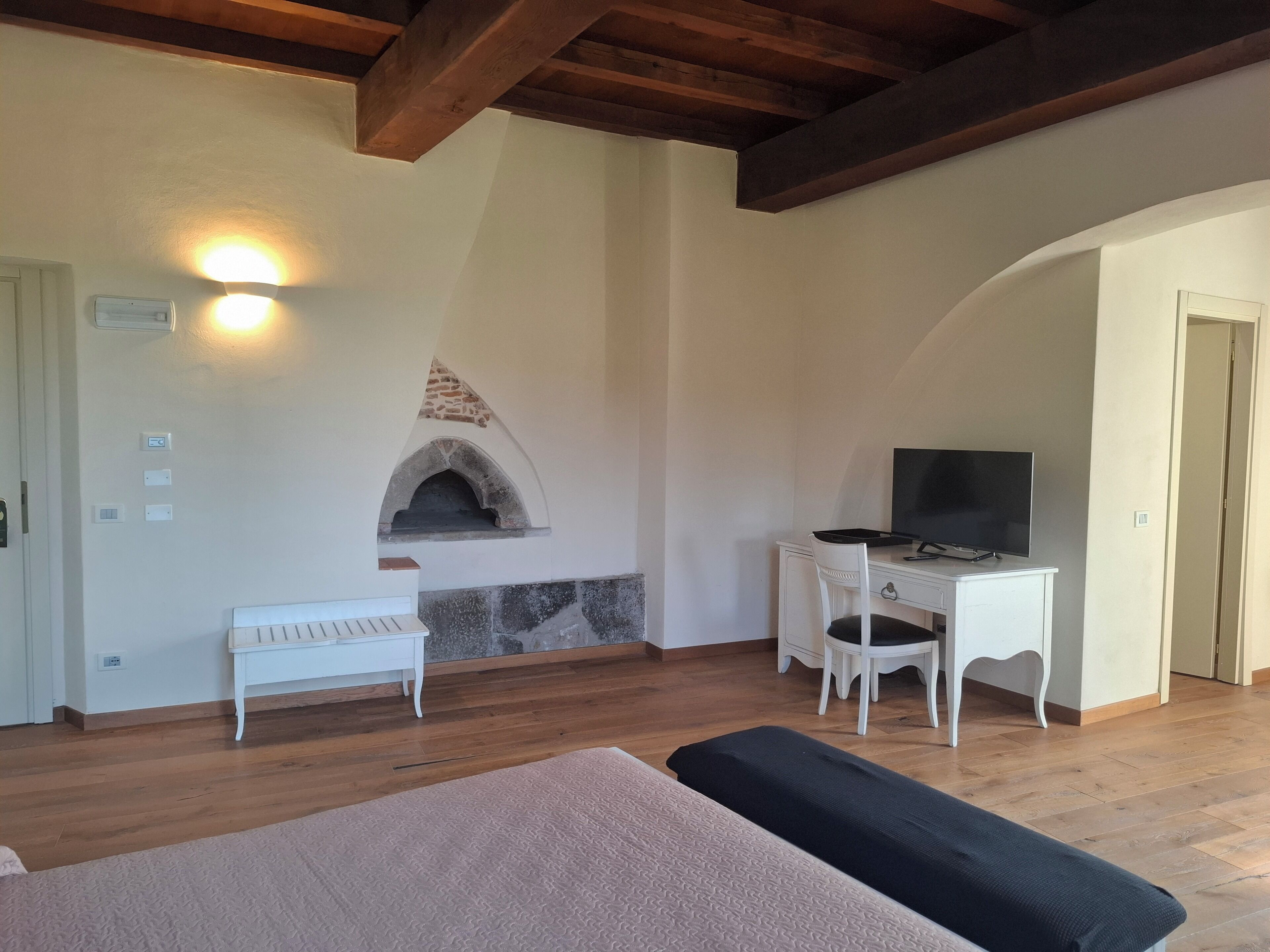 A room with a stone fireplace, a television on a desk, and a bed with a beige cover.