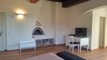 Una habitación con chimenea de piedra, un televisor sobre un escritorio y una cama con cubrecama color beige.