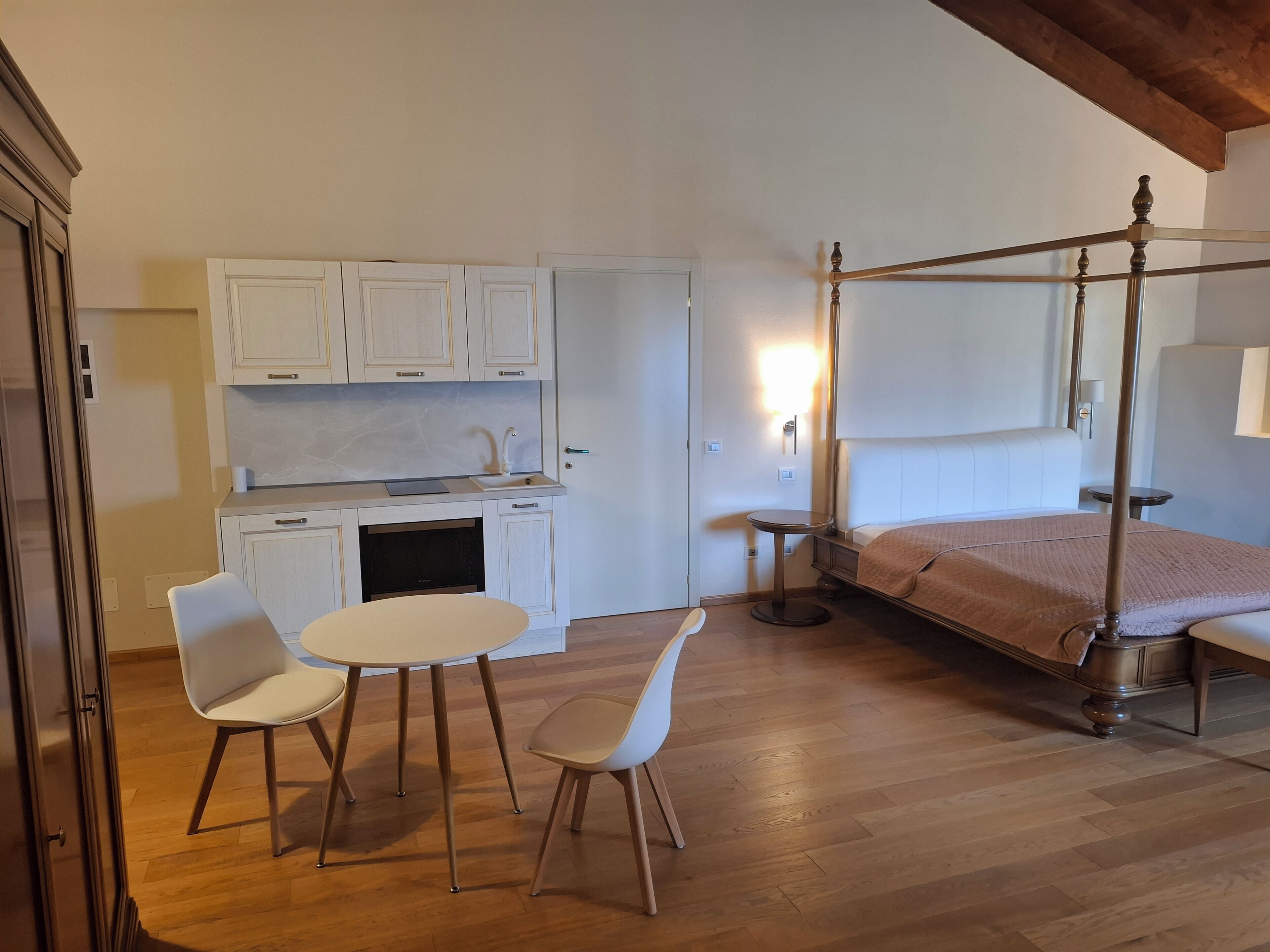 Un dormitori amb un llit amb cortines, una taula rodona petita i dues cadires.