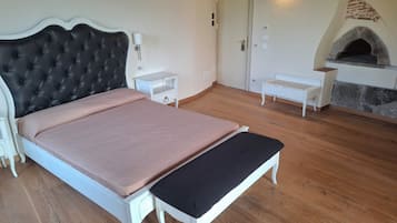 Een slaapkamer met een groot bed, een bankje, een nachtkastje, een open haard en een deur.