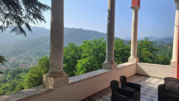 A balcony with a checkered floor, surrounded by columns, overlooking a lush green landscape with distant hills. - Albergo Palazzo Costa (Beverino)