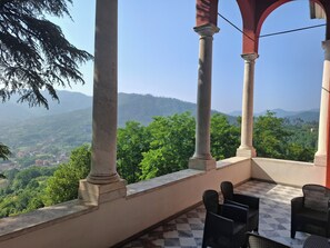 A balcony with a checkered floor, surrounded by columns, overlooking a lush green landscape with distant hills. - Albergo Palazzo Costa (Beverino)