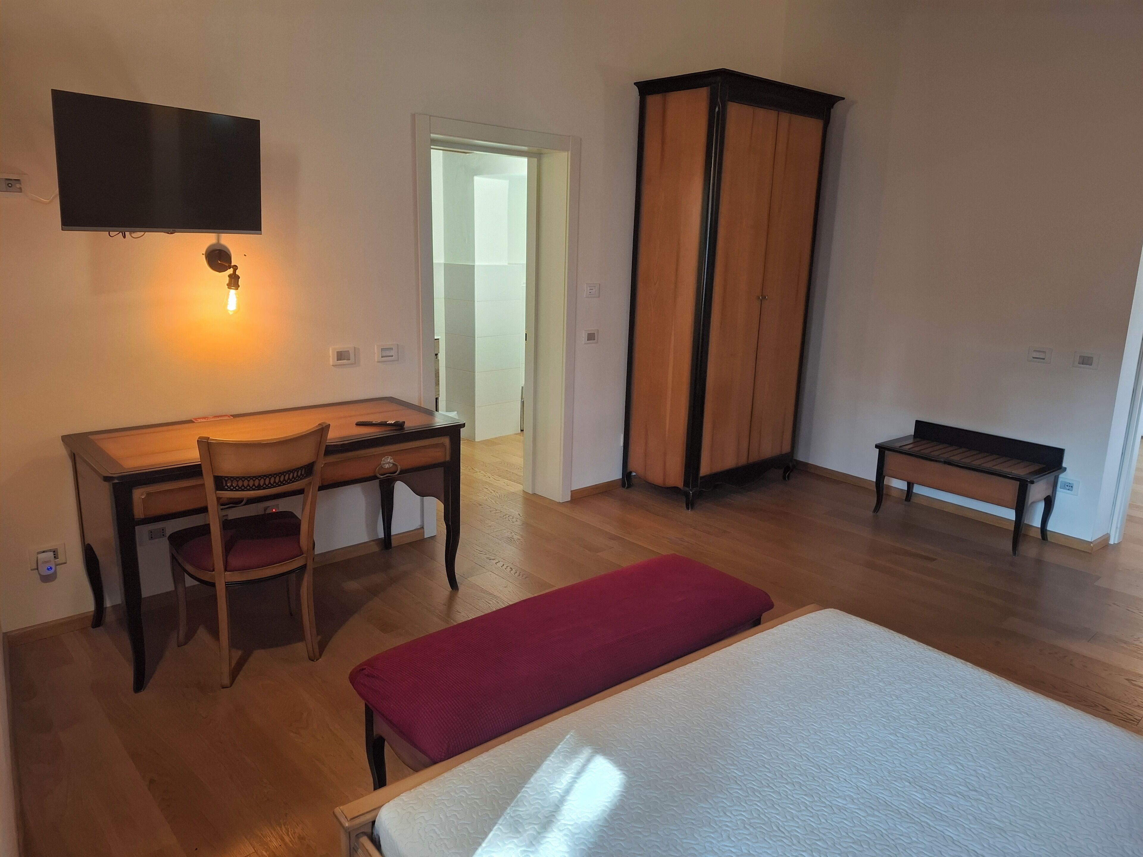 Une chambre à coucher comprenant un lit, un bureau avec une chaise, une armoire et un téléviseur fixé au mur.