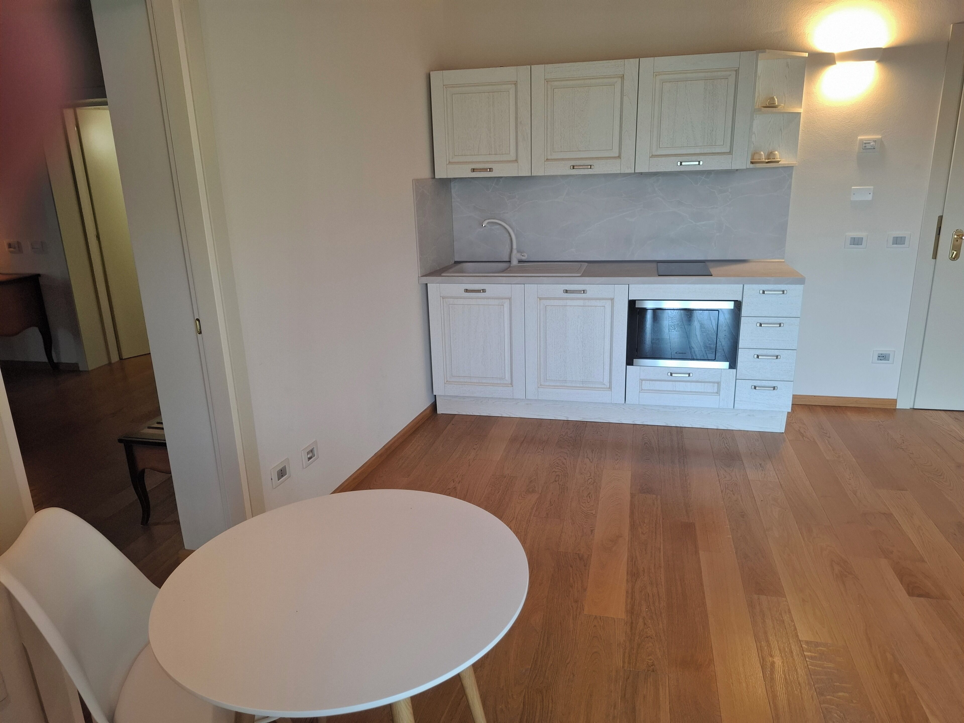 Eine kompakte Küche mit weißen Schränken, einem eingebauten Backofen und einem runden Tisch mit einem Stuhl.