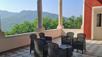 A terrace with checkered flooring, black wicker furniture, and a view of green hills under a clear sky.