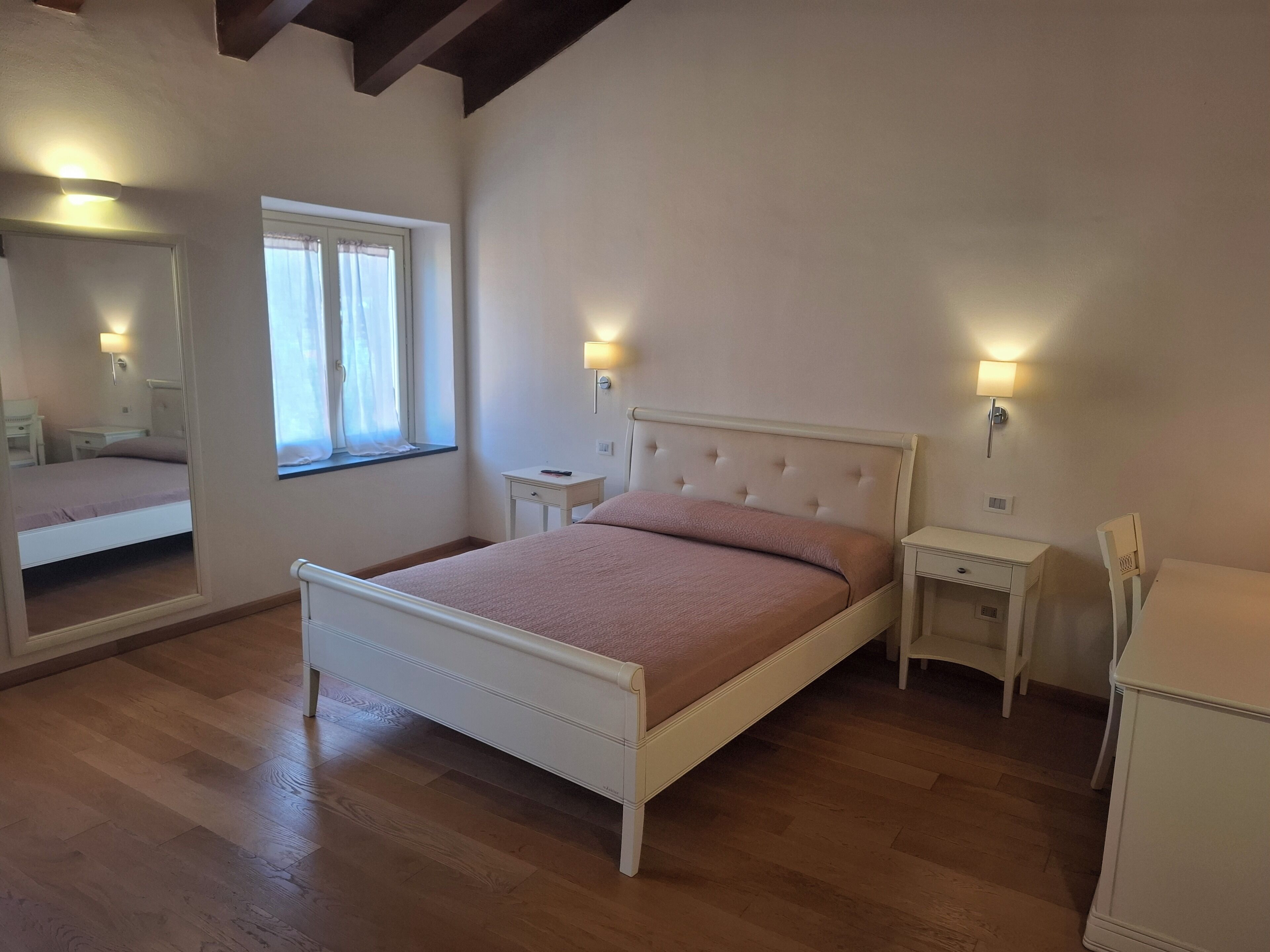 Un dormitorio con cama, mesitas de noche, un espejo y una ventana.