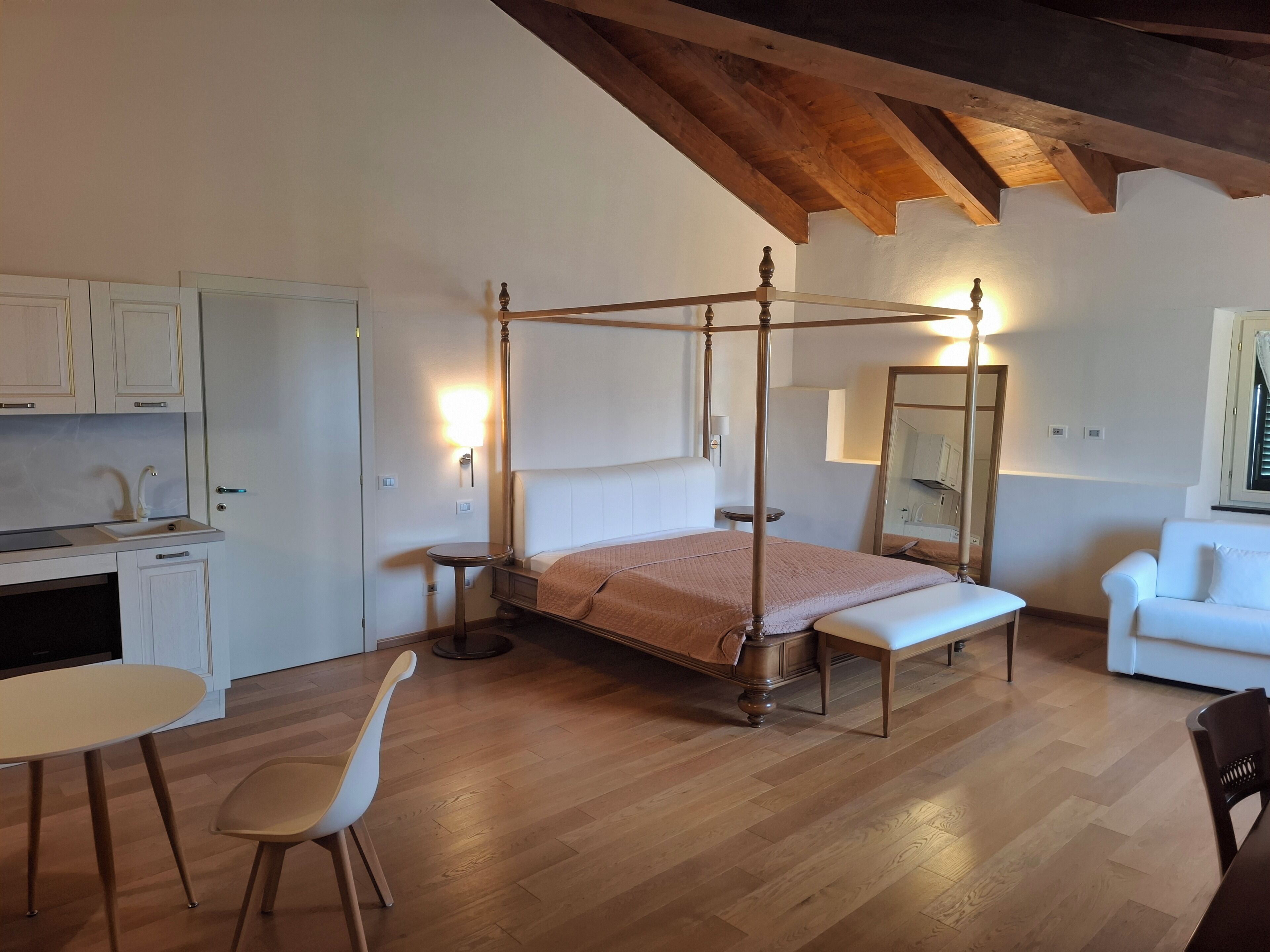Un dormitorio con una cama con dosel, una mesita de noche, una silla, un escritorio con una silla, y un sofá.
