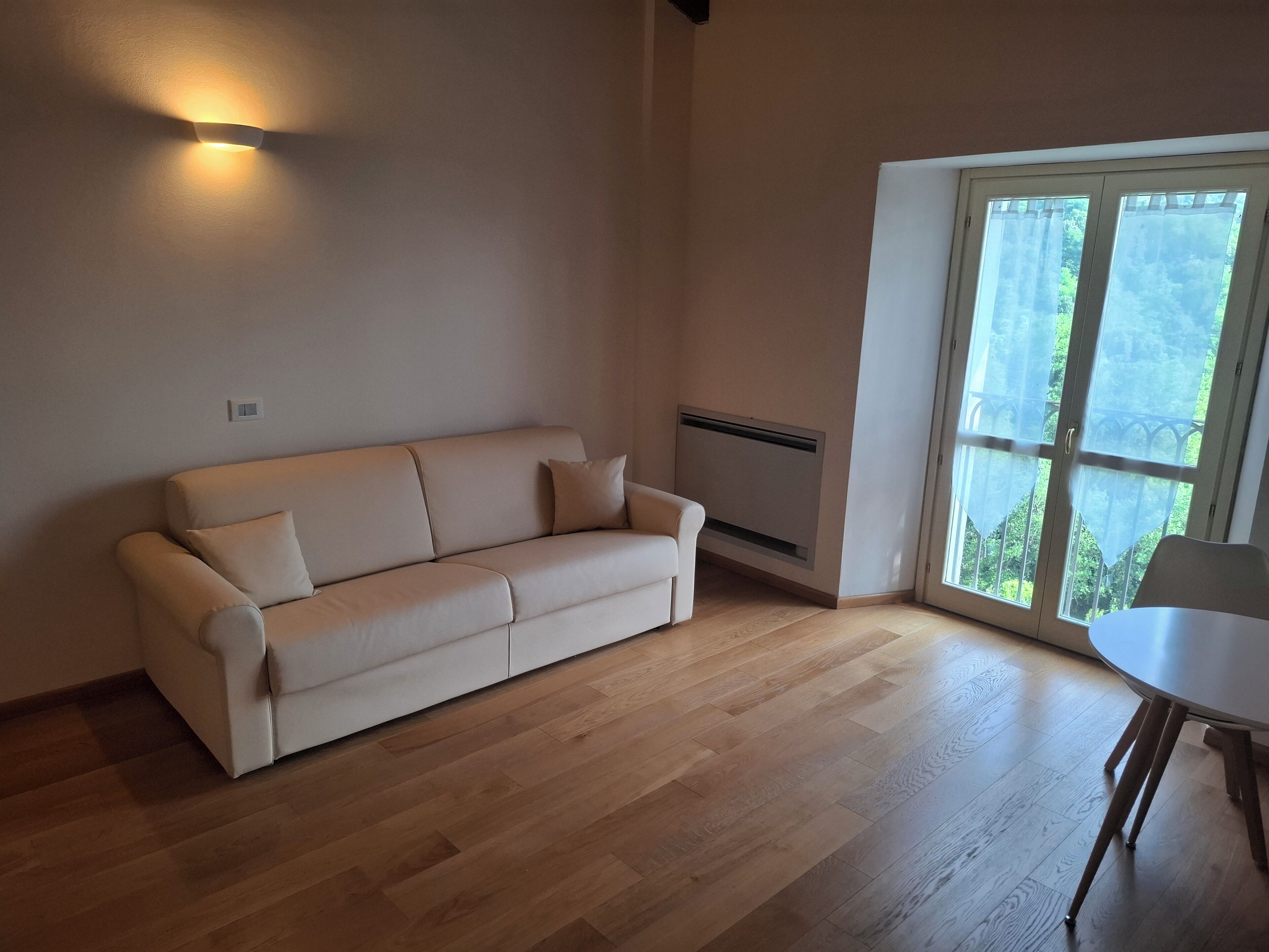 Un salon moderne avec un canapé beige, une petite table et une grande fenêtre donnant sur un paysage verdoyant.