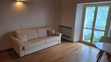Un salon moderne avec un canapé beige, une petite table et une grande fenêtre donnant sur un paysage verdoyant.