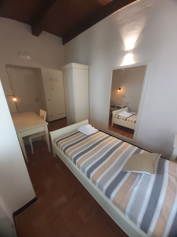 A small, single-room accommodation with a bed, a desk, a chair, and a wardrobe.