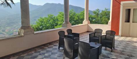 A terrace with checkered flooring, black wicker furniture, and a view of green hills and mountains.
