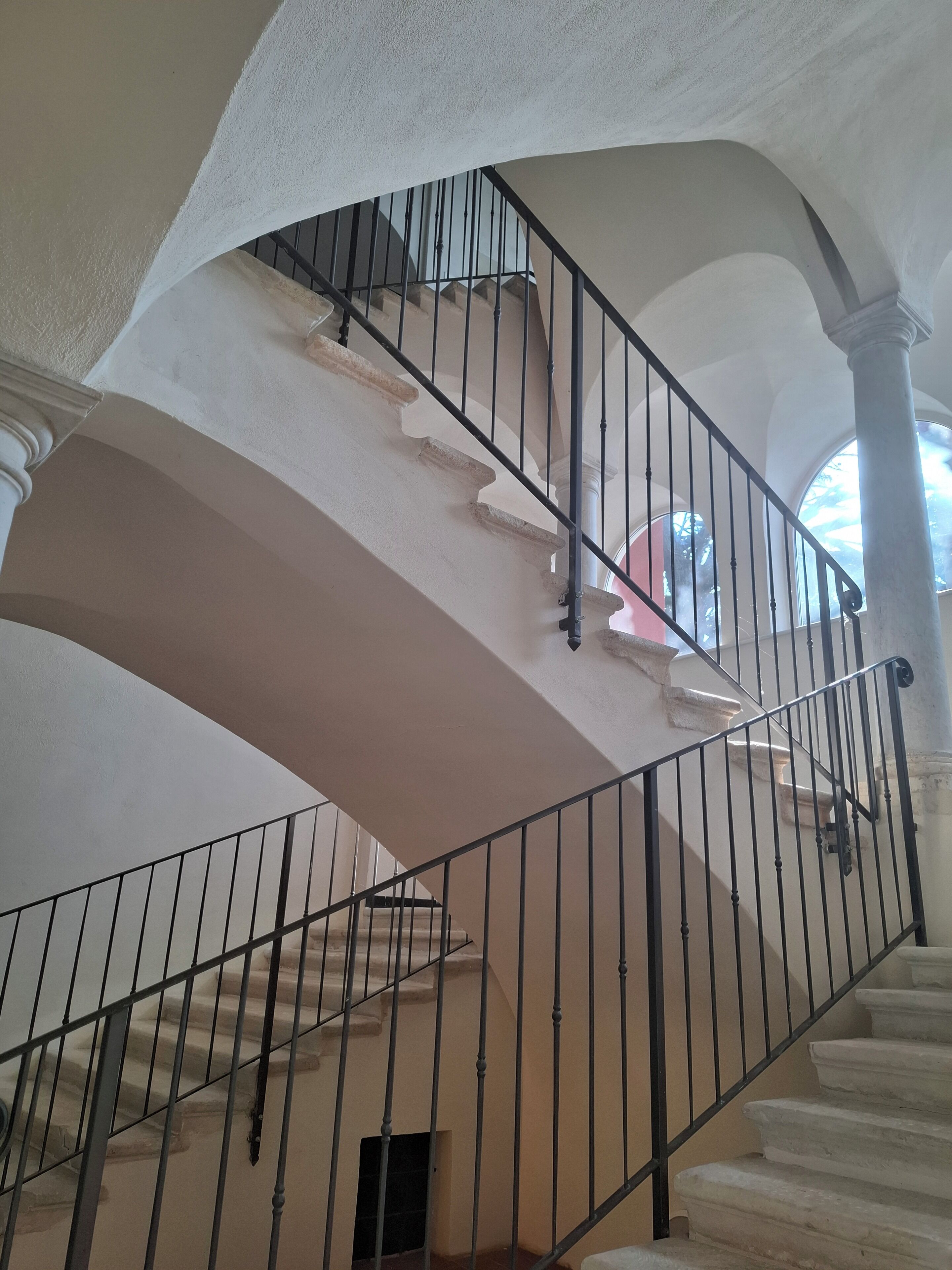 A grand staircase with a curved design, featuring a black metal railing and white walls.