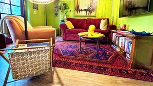 A cozy living room with a red sofa, a patterned armchair, a yellow octopus plush toy, a large rug, and a bookshelf filled with books. - Disco Den on Toad Road (Plainfield)