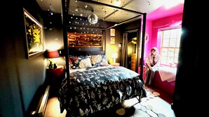 A bedroom with a four-poster bed, a nightstand with a lamp, and a dresser. - Disco Den on Toad Road (Plainfield)