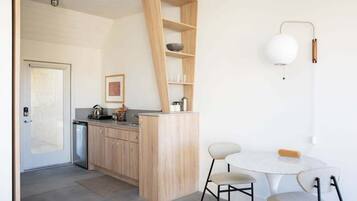 A modern kitchen with wooden cabinets, a built-in shelf, a white table with two chairs, and a pendant light.