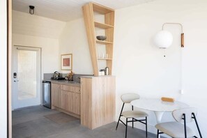 Una cocina moderna con armarios de madera, un estante empotrado, una mesa blanca con dos sillas y una lámpara colgante.