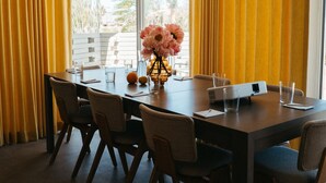 A dining area with a long table, chairs, a vase with flowers, and yellow curtains.