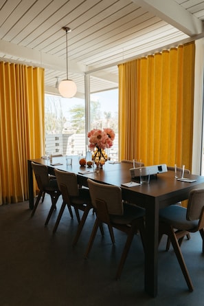 A dining area with a long table, chairs, a vase with flowers, and yellow curtains. - The Bungalows by Homestead Modern, Premium Double (Joshua Tree)