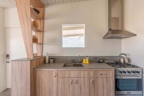 A modern kitchen with wooden cabinets, a stainless steel stove, and a window above the sink. - The Bungalows by Homestead Modern, Premium Double (Joshua Tree)