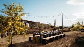An outdoor dining area with tables and benches, a building in the background, and string lights.