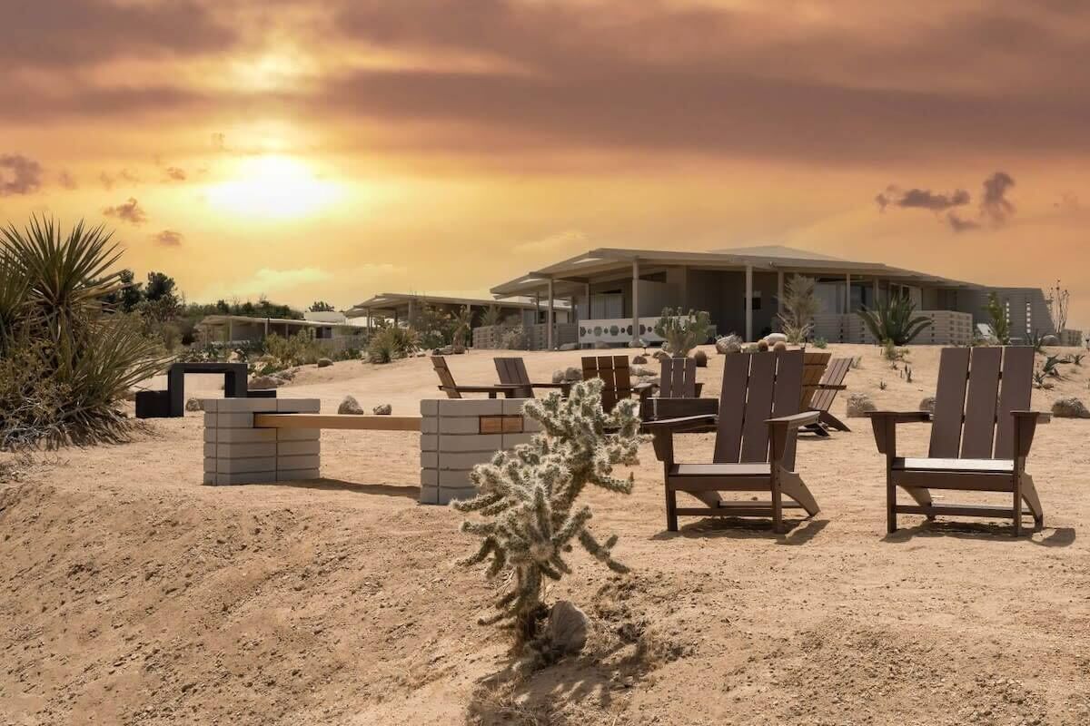 A desert landscape with a modern building, lounge chairs, and a cactus plant.
