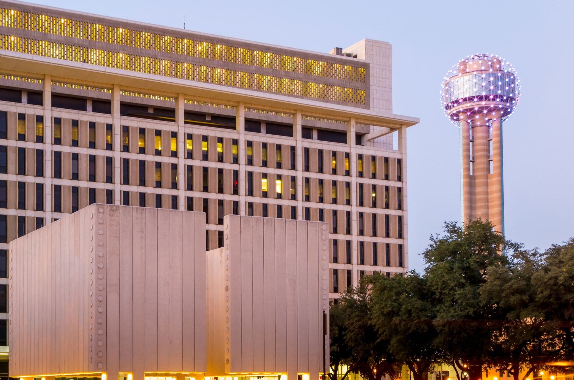 A modern building with a grid-like facade and a spherical tower with lights in the background.