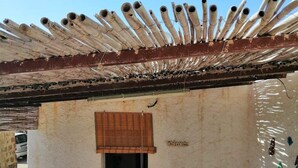 Un espace extérieur abrité, doté d’un toit en métal, d’une porte donnant sur l’intérieur et d’un sol carrelé.