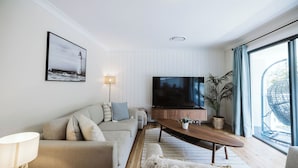 Una sala de estar moderna con un sofá, una mesa de centro, un televisor y un ventanal con cortinas.