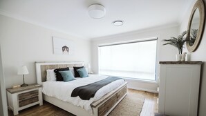 Un dormitorio con cama, mesita de noche y un amplio ventanal.