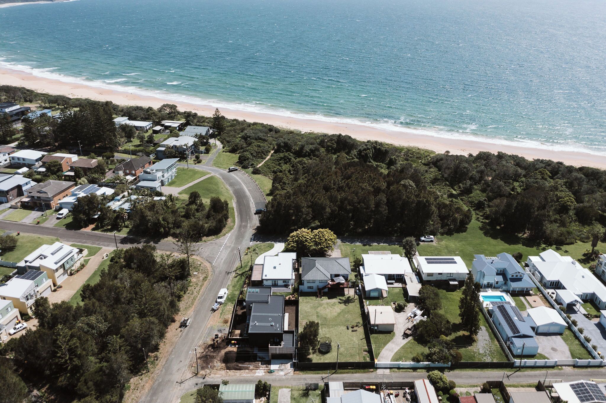 An aerial view of a coastal residential area with houses, a beach, and a road.