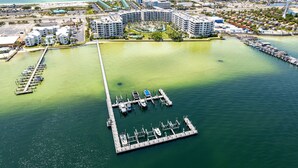 Une vue aérienne d’une marina avec de nombreux quais et des bateaux, entourée d’un complexe hôtelier comprenant plusieurs bâtiments et une plage en arrière-plan.
