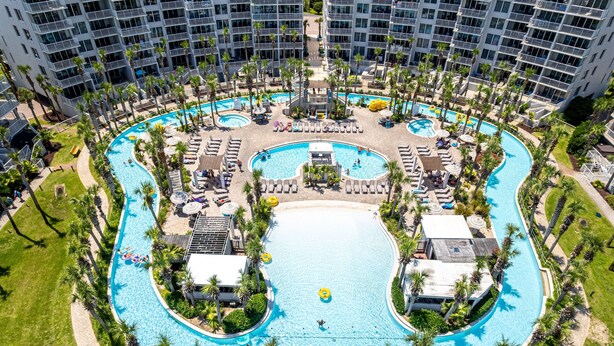 Un grand hôtel à plusieurs étages, doté d’une piscine centrale entourée de palmiers et de chaises longues.