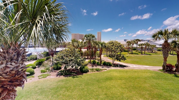 A well-maintained grassy area with palm trees and a clear view of a hotel building in the background. - Mainsail T/h #3 2 Bedroom Townhouse (Miramar Beach)