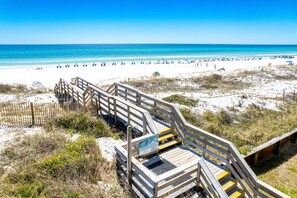 A wooden boardwalk leading to a beach with clear blue water and sandy shore.
