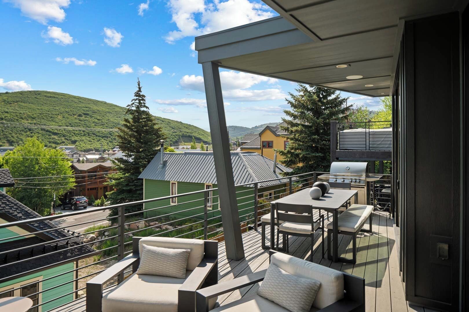 A balcony with outdoor seating, a grill, and a view of a town and hills.