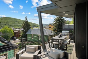 Een balkon met buitenmeubilair, een barbecue en uitzicht op een stad en heuvels.