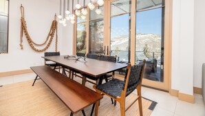 A dining area with a large table, chairs, and a bench. There are hanging lights and a view of a snowy landscape through large windows. - New Remodel Old Town House by InvitedHome | Walk to Town, Ski, Hot Tub, Patio (Park City)